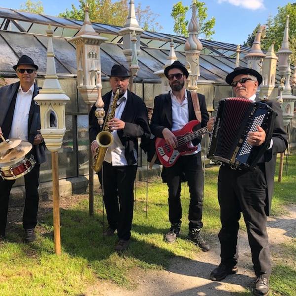 Die Band im schwarzen Anzug vor einem Gewächshaus